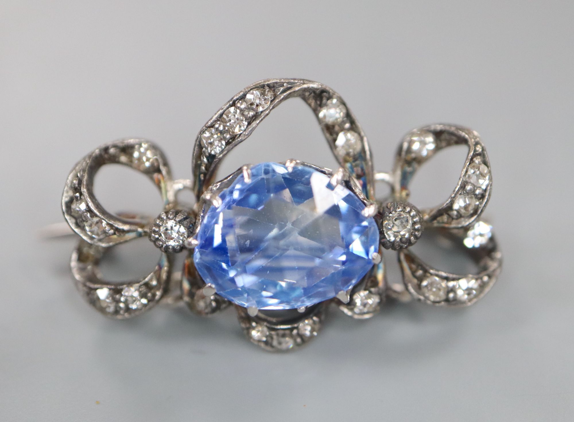 An early 20th century white metal, fancy cut sapphire and diamond chip set scroll pendant brooch, 19mm, gross 4.4 grams.